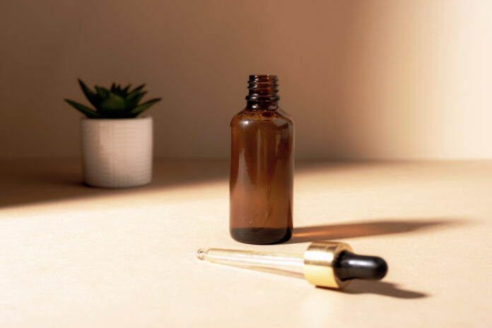 Brown glass cosmetic serum bottle with pipette on light beige background with shadows. Close up