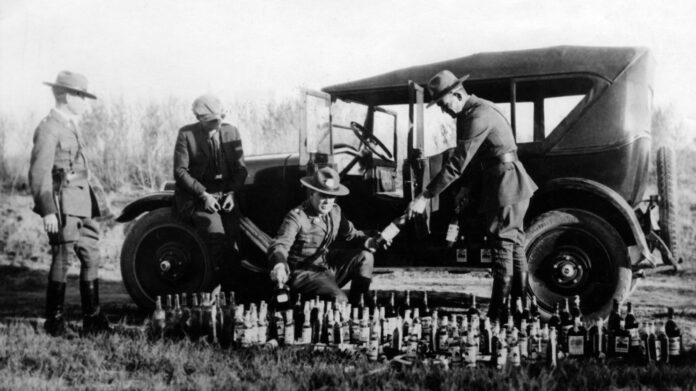Prohibition: Policemen arrest a bootlegger who hid bottles with alcohol in his car at the Mexican boarder.
